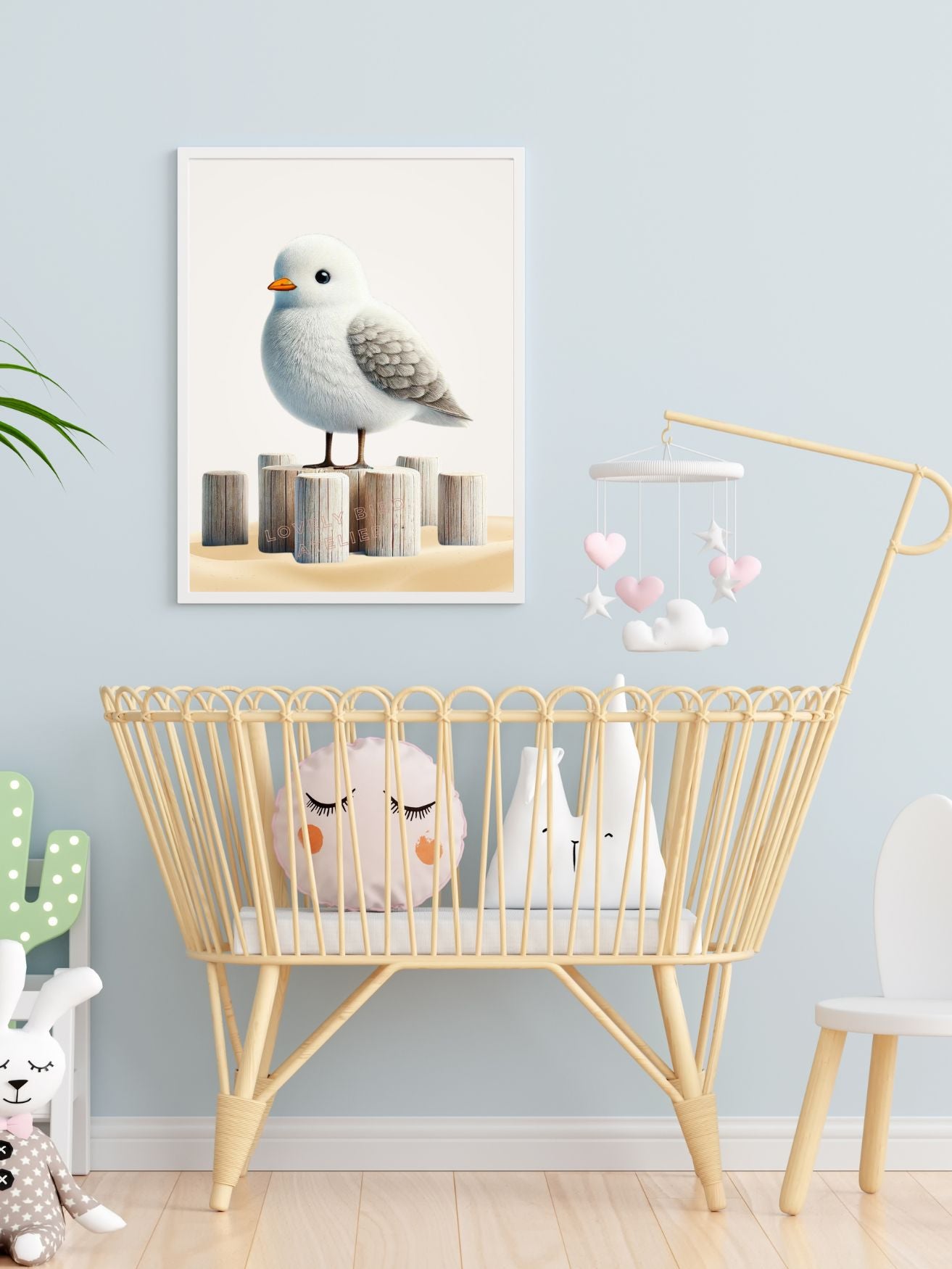 Chambre de bébé avec berceau en rotin, jouets en peluche et mobile en forme de nuages roses, et affiche d'oiseau sur le mur.